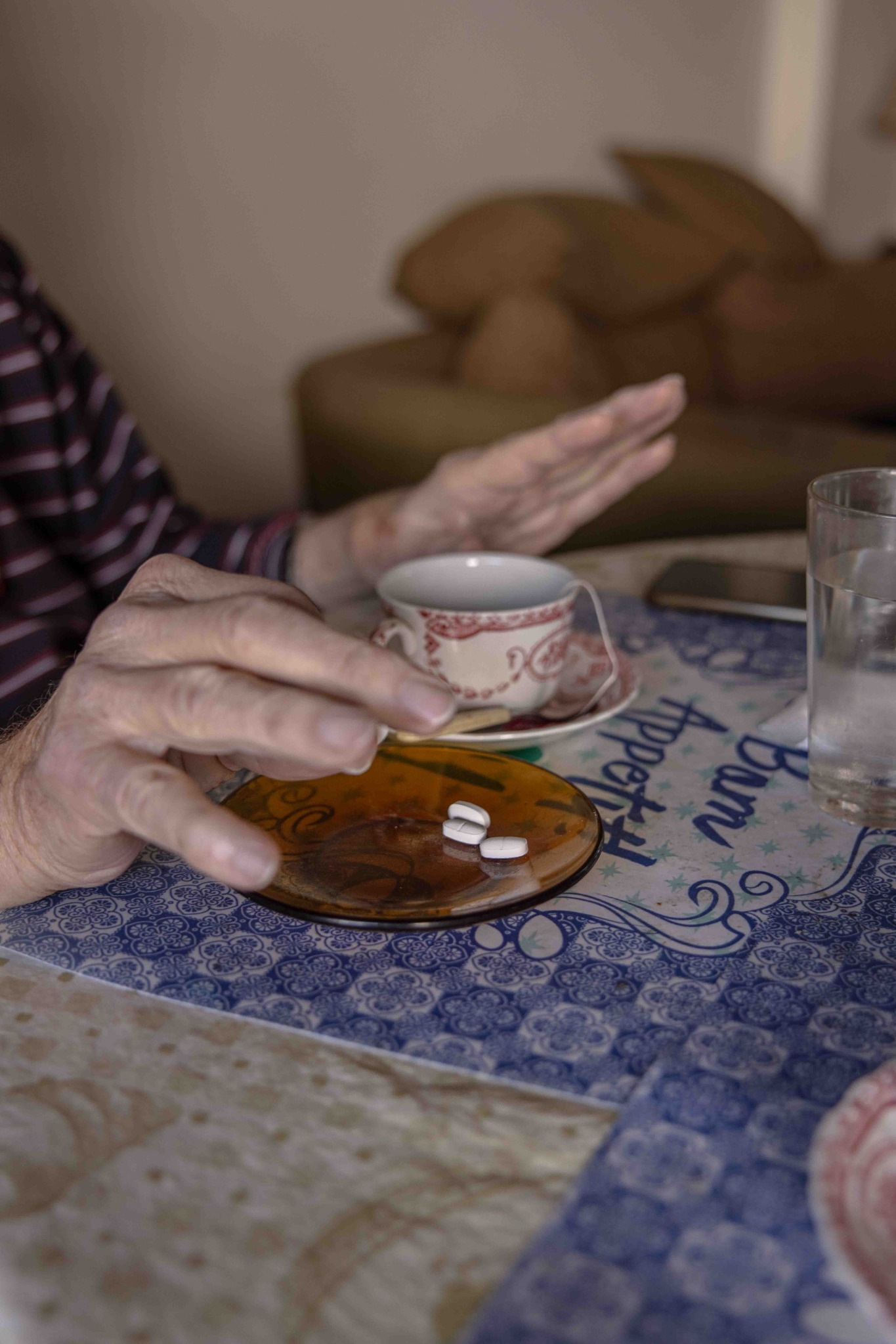 Detalle de una mesa de desayuno con medicamentos y las manos de una persona mayor